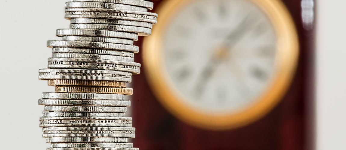 Stacked silver coins with a clock in the background