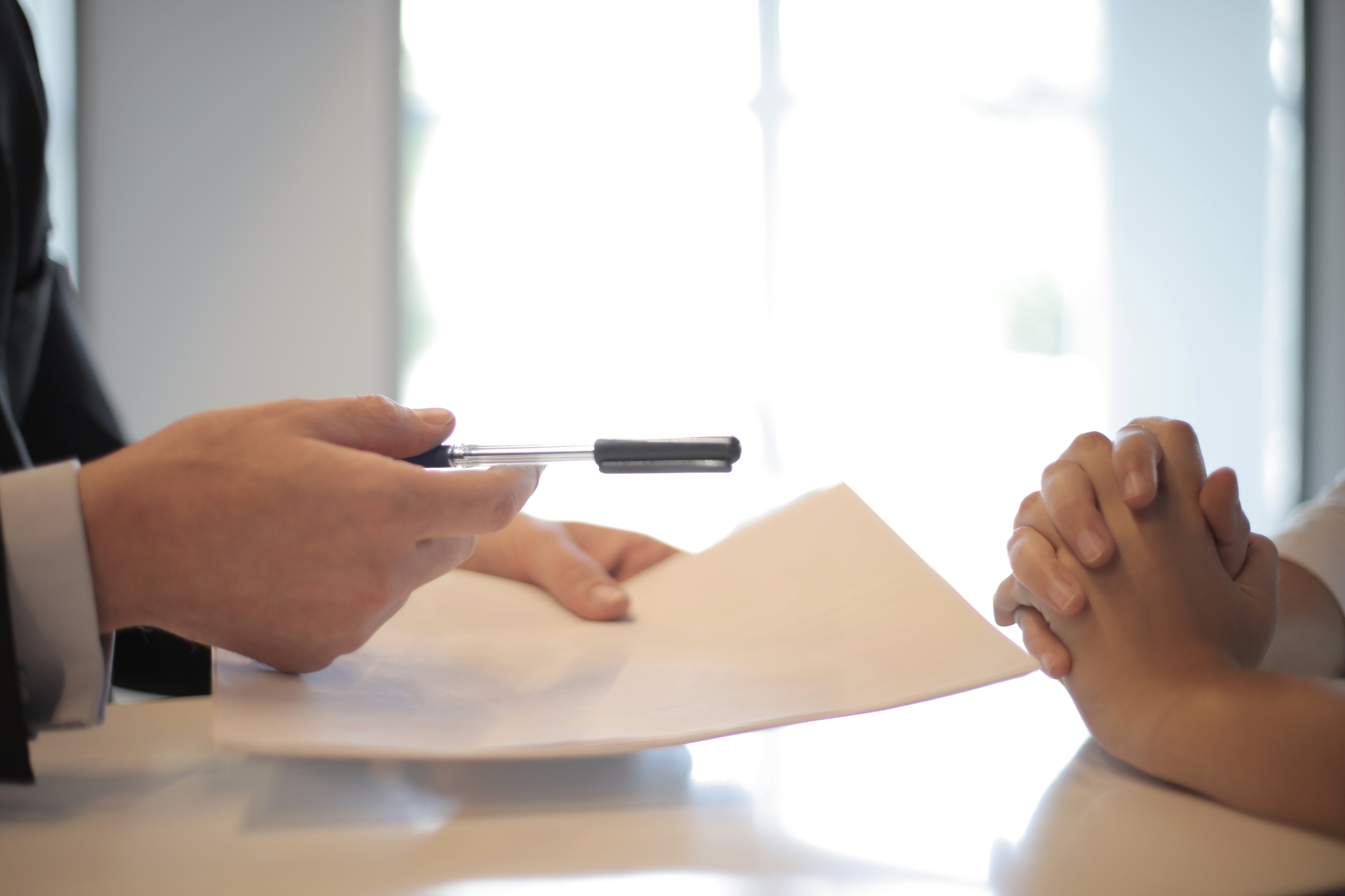 Individual holding out a pen and a stack of papers, like a contract