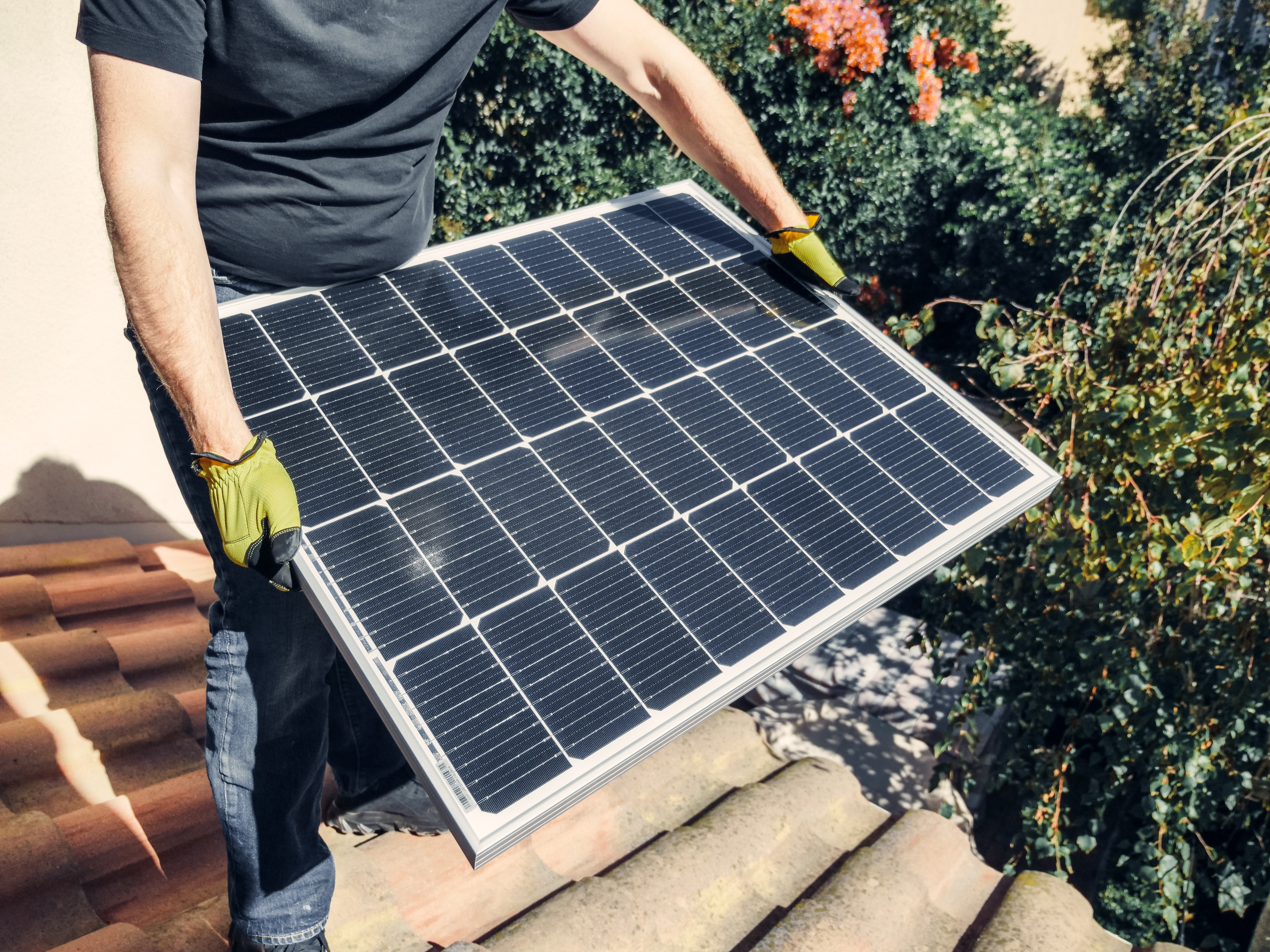 A Person in Black Shirt Holding a Solar Panel while Standing on the Roof