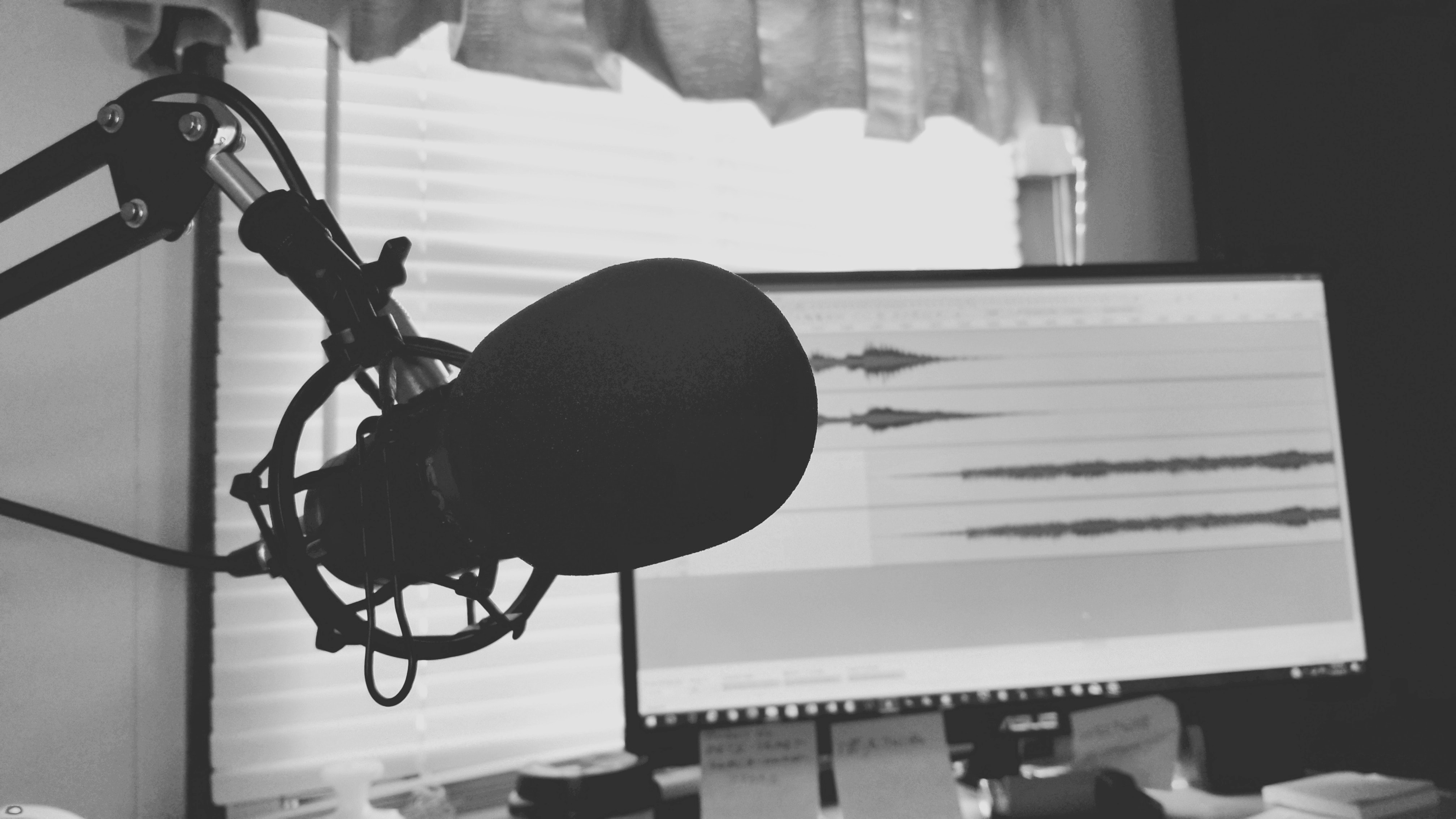 Black and white image of a podcast microphone with sound waves on a laptop in the background