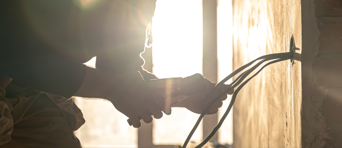 Worker putting wires into a hole with hot sun in the background